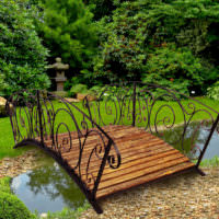 Деревянный мостик с кованными перилами над садовым водоемом